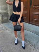 Conjunto sastrero negro de tres piezas: blazer de corte holgado, chaleco cropped con botones y minifalda tableada.