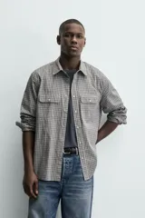 Camisa de corte regular fit confeccionada en tejido de algodón con estampado de cuadros. Presenta cuello solapa, manga larga con puños abotonados, cierre frontal de botones y dos bolsillos de plastrón con solapa en el pecho.