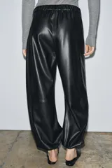 Pantalón bombacho negro de tiro medio, confeccionado en tejido efecto piel, con cintura elástica, bolsillos laterales ocultos y bajo abullonado con elástico.