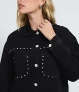 Campera overshirt de jean negro con cuello polo, cierre frontal abotonado, mangas largas y bolsillos delanteros decorados con tachuelas metálicas.