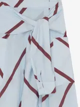 Falda larga cruzada de viscosa y poliamida, color celeste con estampado de líneas diagonales bordó. Presenta silueta amplia, bolsillos laterales y detalle de mangas de camisa incorporadas en la cintura para anudar.