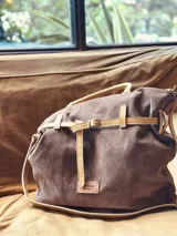 Bolso marrón de cuero gamuza con detalles de correa en cuero mostaza. Tiene una correa corta para llevar como bolso de mano y una correa larga extraíble y regulable. En el interior tiene bolsillo y llavero.