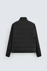 Cazadora acolchada de cuello subido, color negro, con mangas largas de tejido elástico. Incluye bolsillos en la cadera, un bolsillo interior y bajo con elástico. Cierre frontal de cremallera.