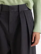 Pantalón de vestir de corte sastrero, con silueta de pata ancha y tiro alto. Presenta un elegante tableado en la cintura delantera, cierre metálico con ganchos y bolsillos laterales y traseros.