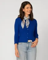 Cardigan blanco de tejido liviano con trama en relieve, cuello a la base y cierre frontal con botones a tono. Presenta mangas tres cuartos.