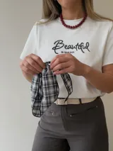 Remera azul marino de manga corta y corte clásico, con estampa bordada con la palabra "Beautiful" en el frente. Incluye un pañuelo de cuello con estampado a cuadros en tonos oscuros.