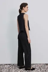Pantalón negro de tiro alto y corte recto, confeccionado con detalles de bordados florales calados en la parte inferior de las piernas.