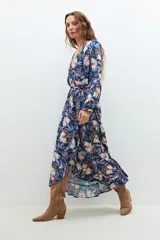 Maxi vestido azul marino con estampado floral en tonos blanco, rosa y azul. Diseño cruzado con lazo en la cintura y mangas largas.