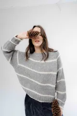 Buzo de tejido de punto grueso en color gris con rayas horizontales en color crema, de corte holgado, cuello redondo y mangas largas.