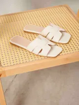 Sandalias planas tipo chinela color camel, con diseño de tiras entrelazadas en forma de "H" y punta cuadrada.