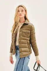 Campera puffer de plumas color beige con diseño acolchado horizontal. Presenta cuello camisero, cierre frontal con broches a presión, bolsillos con solapa en el pecho y bolsillos laterales. Está confeccionada en tejido de poliamida con relleno de plumón y pluma de pato.