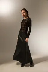 Falda larga de corte evasé confeccionada en cuero sintético negro, con costuras verticales que definen su estructura.