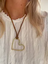 Colgante con dije de corazón calado en metal color bronce, suspendido de un cordón de cuero marrón ajustable mediante un nudo corredizo.