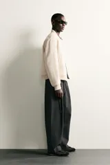 Pantalón de corte balloon fit en color gris oscuro, confeccionado en tejido con viscosa. Presenta pliegues frontales, cintura ajustable con cinturón integrado, bolsillos laterales y bolsillos traseros de doble vivo. Cierre frontal con cremallera y botón.