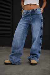 Jean de tiro medio con corte recto y holgado, confeccionado en denim azul. Presenta un diseño con estrellas bordadas en color oscuro a lo largo de las costuras laterales.