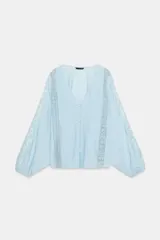 Blusa de escote en pico con cierre frontal de botones, mangas largas abullonadas con bordados a contraste y detalles de encaje tipo entredós y jaretas en el frente.