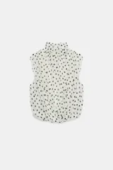 Blusa sin mangas blanca con estampado de lunares negros, cuello alto drapeado y nudo frontal en el bajo.