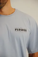Remera de algodón color celeste, de corte holgado y manga corta. Presenta un estampado gráfico pequeño en el pecho con la frase 'Growing like a flower'.