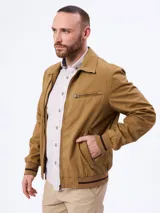 Campera tostada con cierre frontal, bolsillos laterales con cierre y un bolsillo adicional en el pecho. Cuenta con cuello clásico y puños y cintura elastizados con líneas oscuras contrastantes.