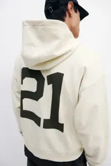 Canguro de algodón pesado color beige, con capucha de doble capa, hombros caídos y bolsillo canguro. Puños y bajo en punto acanalado. Estampado frontal con el número "21" en color negro.