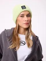 Gorro tipo beanie de punto acanalado en color lila, con parche rectangular negro en el frente que incluye la inscripción 'EAT THE WAVE'.