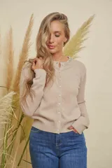 Saco de punto color beige, con cuello redondo y cierre frontal de botones brillantes. El cuello está decorado con apliques de strass.