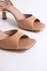 Sandalia de vestir color nude, con punta cuadrada, tira ancha sobre los dedos y pulsera al tobillo con hebilla dorada.