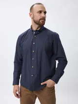 Camisa de manga larga con estampado de cuadros pequeños en tonos azul marino y blanco. Presenta cuello clásico con botones, cierre frontal abotonado y puños ajustables.