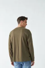 Remera verde militar de manga larga con cuello redondo y estampado frontal con la frase "Create the adventure".