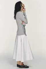 Vestido midi de cuello redondo y manga larga, con la parte superior gris y la falda blanca. La parte superior presenta un detalle de tejido superpuesto ajustable con lazada en la cintura. La falda es de tipo gabardina.