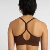 Top deportivo New Balance de soporte ligero, diseñado para yoga y actividades de bajo impacto. Presenta un diseño de estilo jersey con tirantes finos y espalda cruzada, banda elástica inferior para mayor ajuste y logo de la marca en el frente.