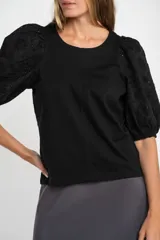 Remera de algodón color rosado con mangas cortas abullonadas de broderie con diseño floral calado. Presenta cuello redondo y costura vertical central en el frente.