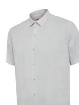 Camisa de manga corta color gris, confeccionada en lino orgánico. Presenta cuello clásico, cierre frontal con botones y un pequeño logo bordado en el pecho.
