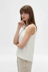 Musculosa blanca sin mangas de viscosa, con cuello asimétrico y detalles bordados en tono sobre tono.