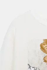 Sudadera de cuello redondo y manga larga, con diseño de estampado artístico metalizado en tonos dorados y plateados en el frente. Presenta acabados en rib en cuello, puños y ruedo.
