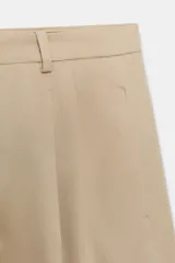 Pantalón de tiro medio con corte wide leg, confeccionado en algodón. Presenta cintura con trabillas, bolsillos laterales ocultos y detalle de pliegues en el delantero. Cierre frontal con cremallera, botón y ganchos metálicos.