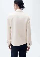 Blazer de corte recto y diseño estructurado, color crema, con cuello de solapa con muesca y cierre frontal de doble botonadura con botones en contraste. Cuenta con dos bolsillos de ribete frontales y mangas largas.