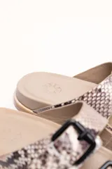 Sandalias de cuero color negro con dos tiras anchas sobre el empeine, cada una con hebillas metálicas ajustables y detalles de tachas plateadas. La suela es de cuero con un borde de color madera.