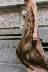 Vestido midi satinado de color marrón, con cuello fluido y diseño sin mangas. Presenta un cierre en la espalda con botones y una falda fluida con sutiles pliegues.