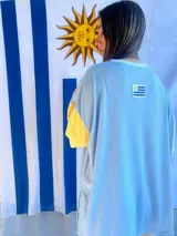Remera de corte oversize confeccionada en tejido de punto acanalado color celeste, con mangas cortas en color amarillo y detalle de parche bordado con la bandera de Uruguay en la parte superior de la espalda.