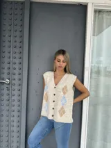 Chaleco tejido de punto con escote en V y cierre frontal de botones. Presenta un diseño de rombos en tonos beige y celeste sobre una base color crema.