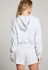 Campera gris con capucha, cierre frontal y detalles de flechas marrones en el pecho y los hombros.