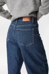 Jean de corte wide leg y tiro alto, confeccionado en denim azul con sutil textura rayada vertical. Presenta diseño de cinco bolsillos, cierre frontal con botón y costuras reforzadas.