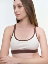 Top deportivo de microfibra en color beige con detalles de ribetes y banda inferior en color marrón. Presenta diseño de espalda estilo nadadora y logo de la marca estampado en la banda elástica inferior.
