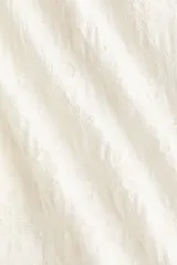 Pantalón blanco de punto con diseño texturizado estilo encaje, de corte holgado con piernas globo, cintura elástica con cordón ajustable y bajos con elástico.