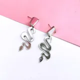 Par de aros colgantes con forma de serpiente plateada y pieza geométrica rosada en la parte superior.