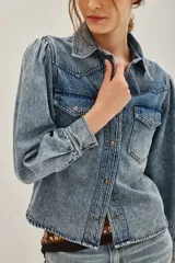 Camisa de jean de corte clásico con efecto lavado, cuello camisero, cierre frontal con botones metálicos y bolsillos frontales con solapa. Presenta mangas largas con diseño abullonado en los hombros y puños abotonados.