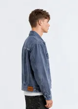 Chaqueta de jean estilo boxy, con corte amplio y cuadrado, solapas clásicas, cierre frontal de botones metálicos, bolsillos frontales con solapa y detalles desflecados en los bordes.