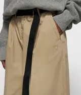 Pantalón de corte clásico y pernera muy ancha, color beige claro, con cintura elástica y cinturón de tela negro con logo bordado.