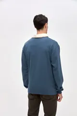 Remera polo de manga larga en color azul, confeccionada en algodón pesado con textura suave. Presenta cuello camisero en color crema, cierre frontal con botones y puños en las mangas. Incluye un pequeño bordado en el pecho.